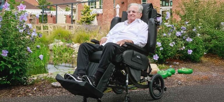 A tall man sits in a comfortable, modern wheelchair specifically designed for extra legroom.
