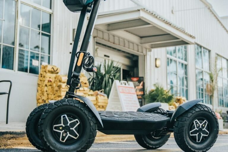 A modern four-wheel electric scooter parked on a bright urban plaza.
